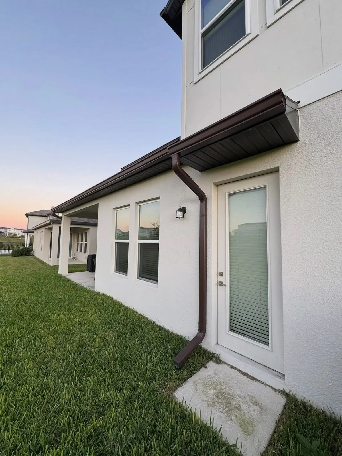 Dark bronze gutter and downspout on a stucco home at sunset