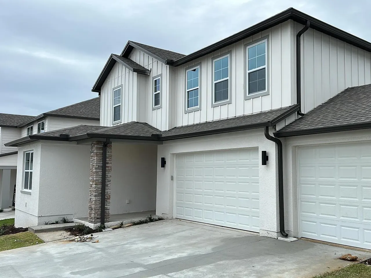 Two-story white board-and-batten home with black seamless gutters and downspouts