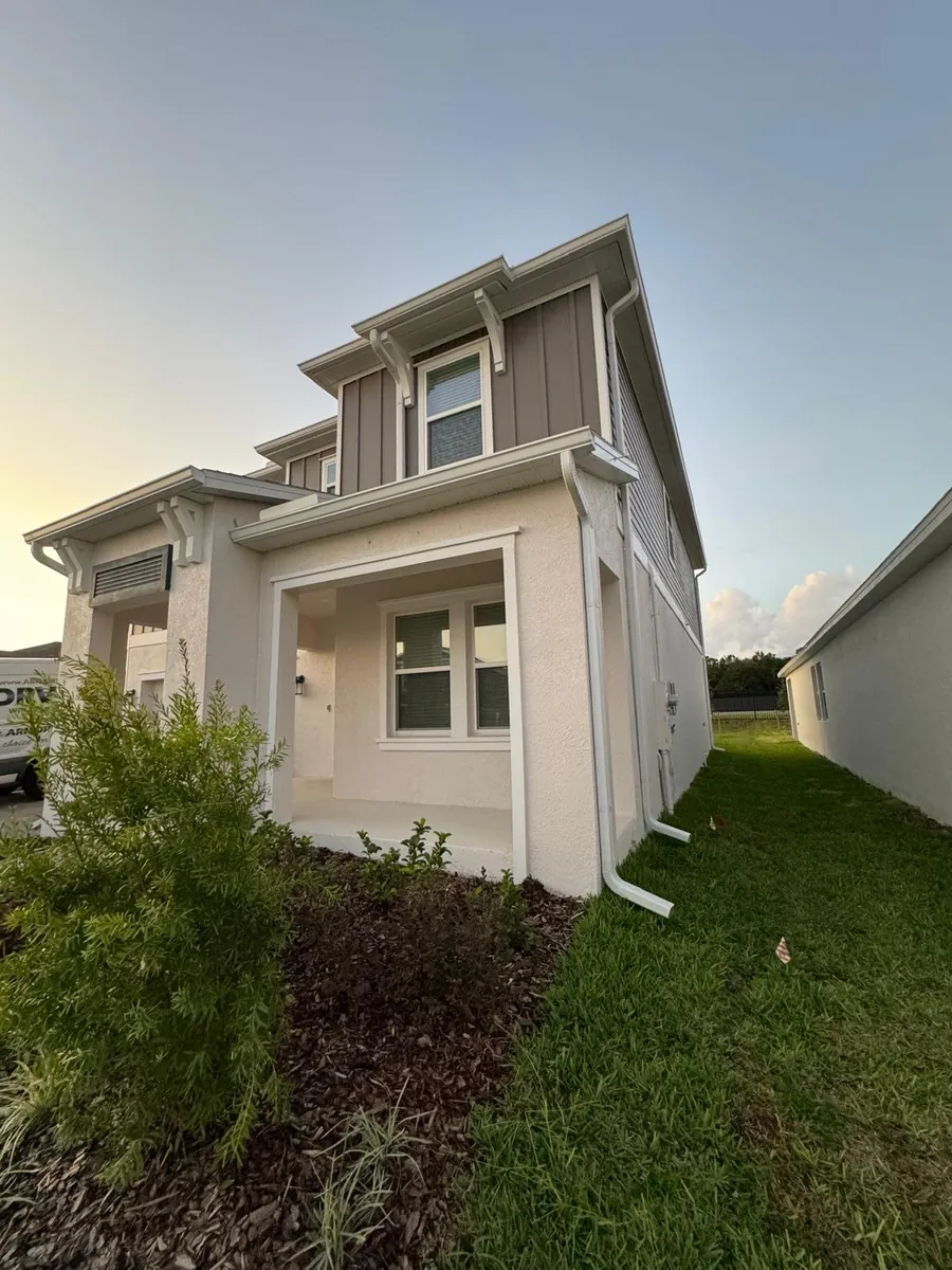 Two-story beige home with a white downspout on the side elevation