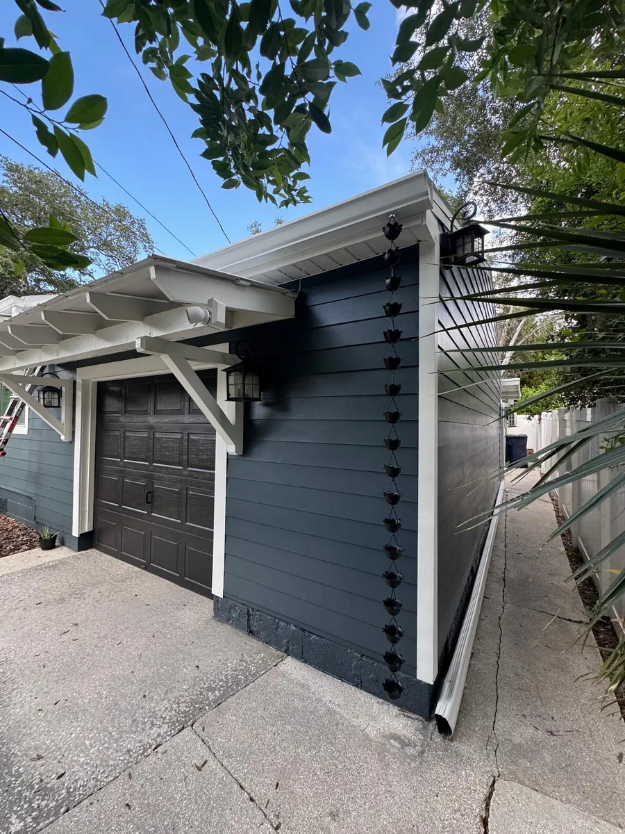 Detached garage with dark siding, white gutter and a rain chain