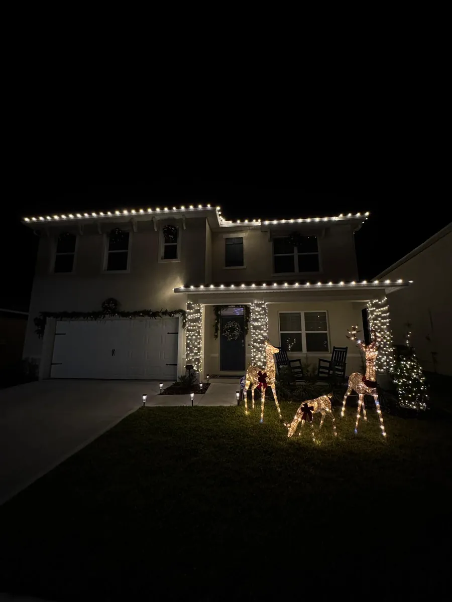 Two-story home at night with warm white roofline lights and lit reindeer