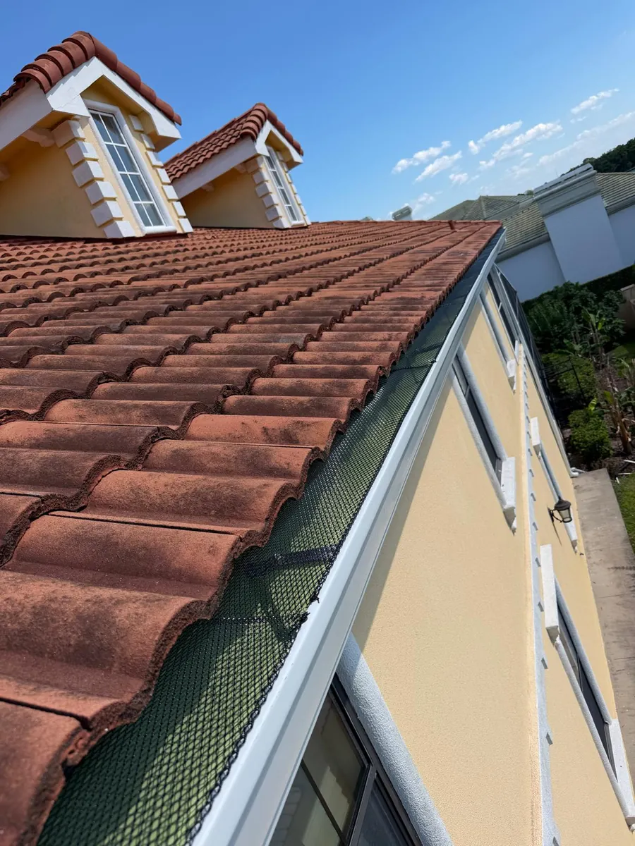 Gutter guard along a terracotta tile roof on a two-story home