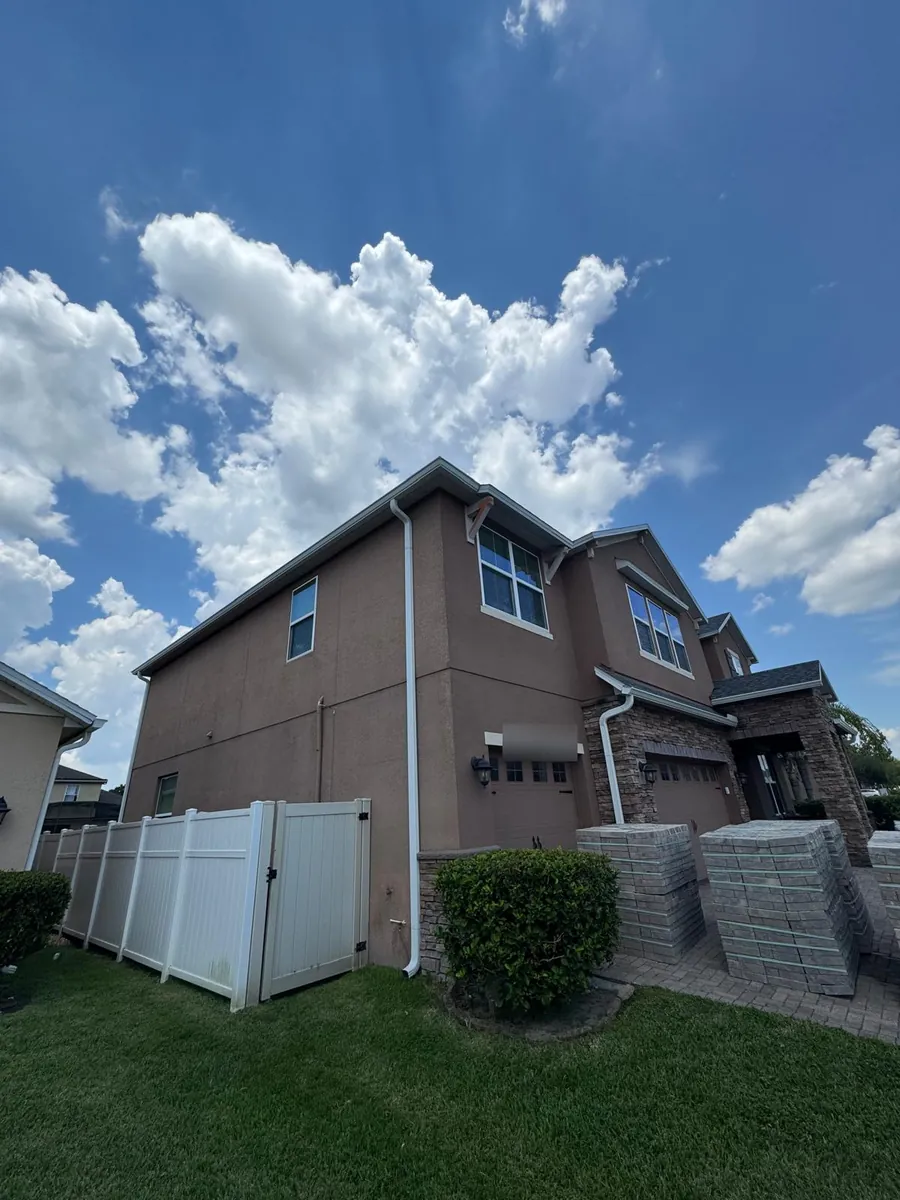 Two-story brown stucco townhome with white gutters and downspouts
