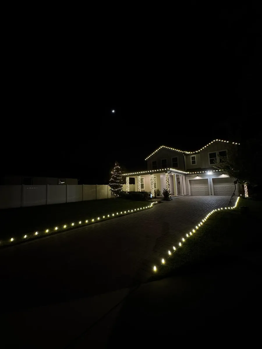 Home at night with warm white roofline, wrapped columns, lit tree and driveway lights